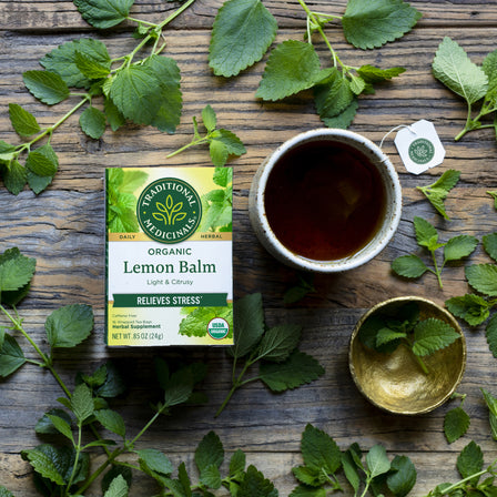 Box of lemon ginger tea alongside a cup and ginger leaves on a wooden surface, perfect for promoting healthy digestion.