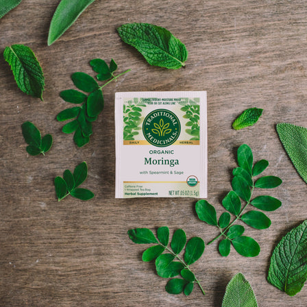 A box of Moringa with Spearmint & Sage Tea features leaf illustrations and is situated on a wooden surface.